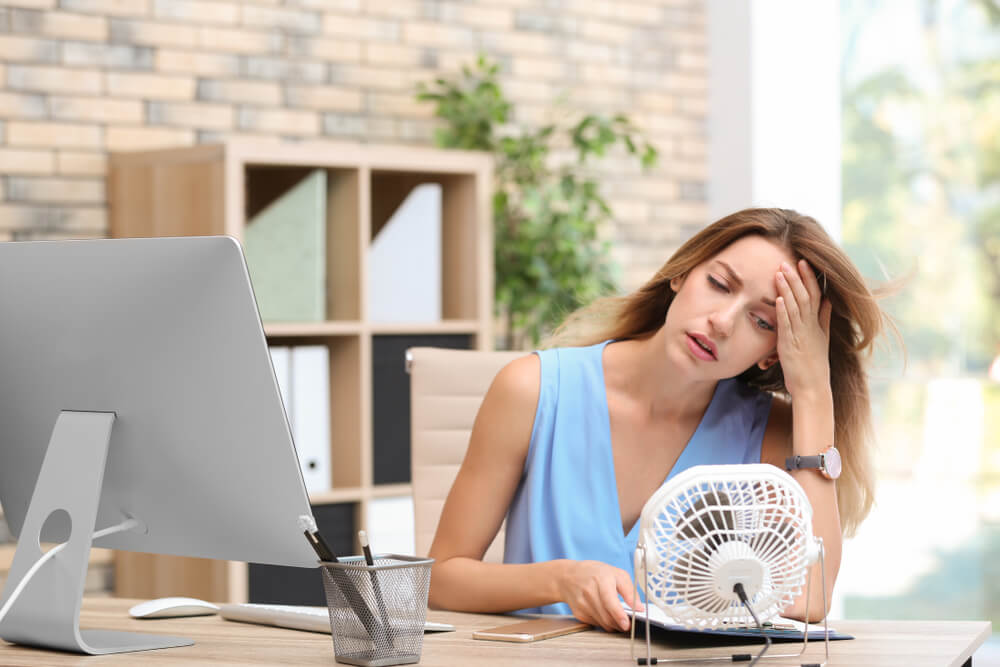 Žena před monitorem počítače, která se ochlazuje u ventilátoru